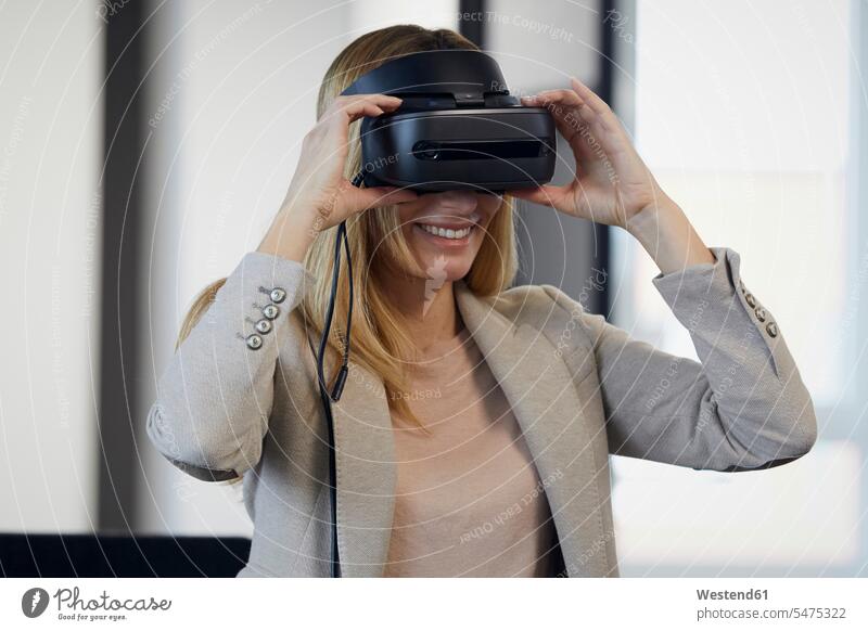 Lächelnde Geschäftsfrau mit VR-Brille im Büro Job Berufe Berufstätigkeit Beschäftigung Jobs geschäftlich Geschäftsleben Geschäftswelt Geschäftsperson