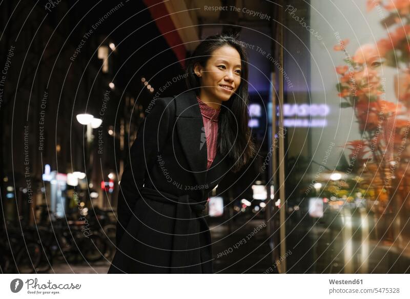 Lächelnde junge Frau, die nachts in ein Schaufenster schaut, Frankfurt, Deutschland geschäftlich Geschäftsleben Geschäftswelt Geschäftsperson Geschäftspersonen