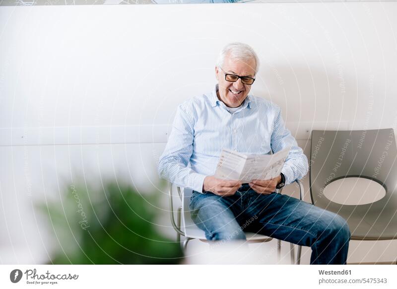Älterer Mann sitzt im Wartezimmer einer Arztpraxis und liest ein Faltblatt Leute Menschen People Person Personen Europäisch Kaukasier kaukasisch 1 Ein
