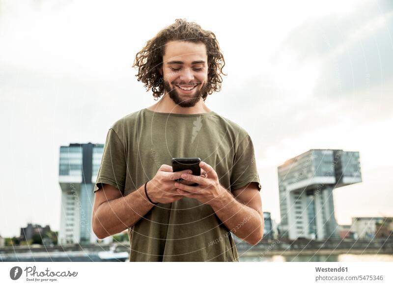 Deutschland, Köln, lächelnder junger Mann schaut auf Handy ansehen Mobiltelefon Handies Handys Mobiltelefone schauen sehend Telefon telefonieren Kommunikation