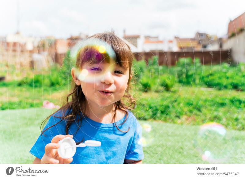 Porträt eines glücklichen kleinen Mädchens, das in einem Park Seifenblasen bläst T-Shirts blasend pusten wehen fliegend Jahreszeiten Frühjahr Lenz sommerlich