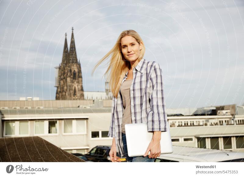Deutschland, Köln, Porträt einer lächelnden blonden Frau mit Laptop Portrait Porträts Portraits weiblich Frauen blonde Haare blondes Haar Erwachsener erwachsen