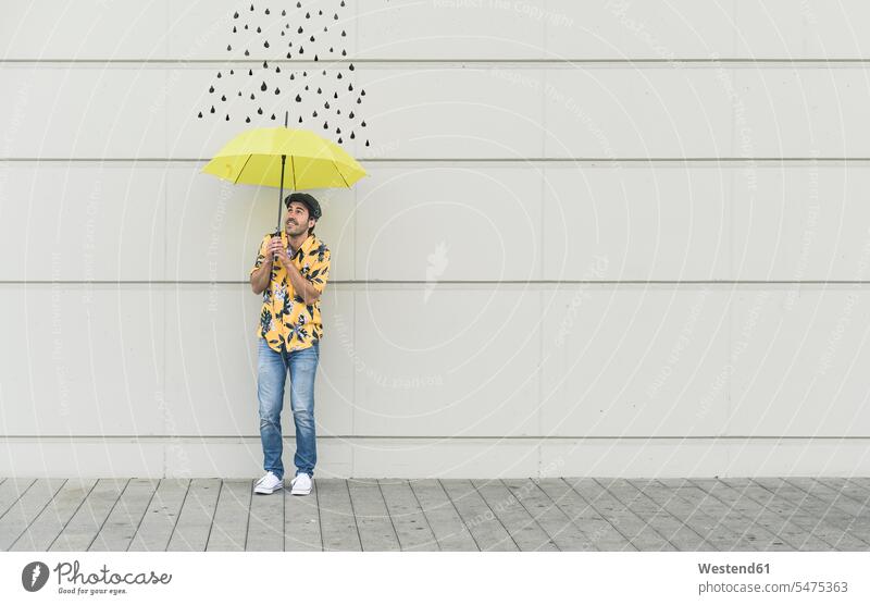 Digitales Komposit eines jungen Mannes, der einen Regenschirm an eine Wand mit Regentropfen hält Leute Menschen People Person Personen Europäisch Kaukasier