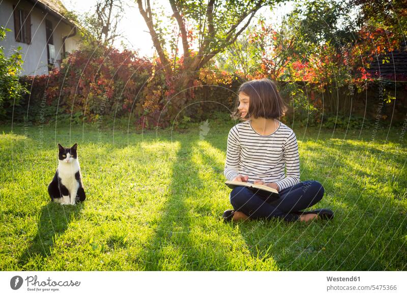 Lächelndes Mädchen sitzt auf der Wiese mit einem Buch neben der Katze lächeln Kind Mensch Haustier Tier Außenaufnahme ein Tier Natur Freude Textfreiraum