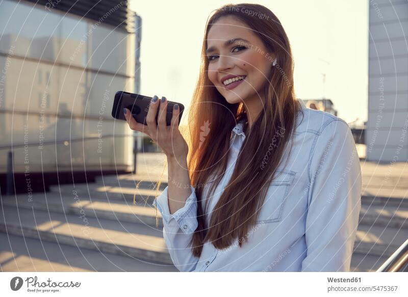 Lächelnde Geschäftsfrau, die mit dem Handy spricht, während sie auf Stufen steht Farbaufnahme Farbe Farbfoto Farbphoto Außenaufnahme außen draußen im Freien