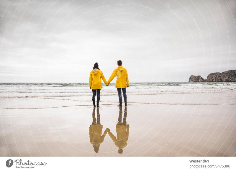Junge Frau in gelben Regenjacken und am Strand stehend, Bretagne, Frankreich Mützen gefühlvoll Emotionen Empfindung Empfindungen fühlen Gefühl Gefühle lieben
