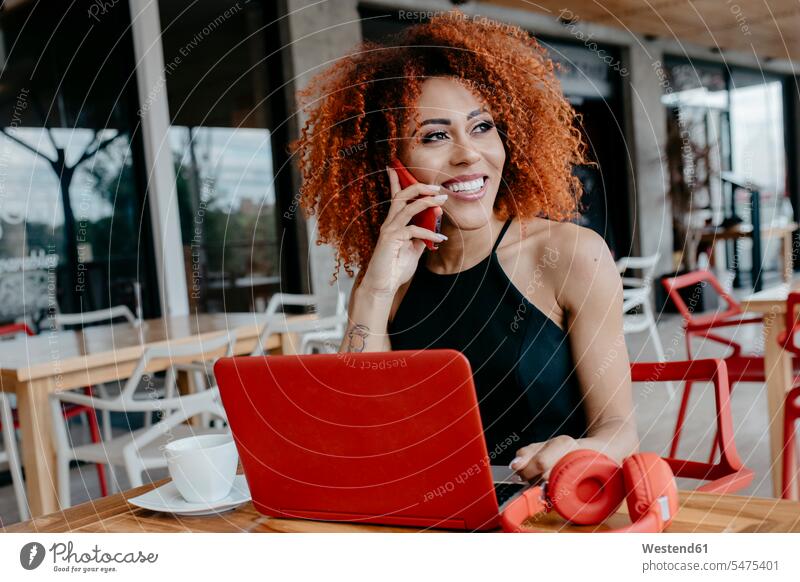 Afro-Frau mit Laptop und Kopfhörern auf dem Tisch, die sich im Straßencafé über ein Smartphone unterhält Farbaufnahme Farbe Farbfoto Farbphoto