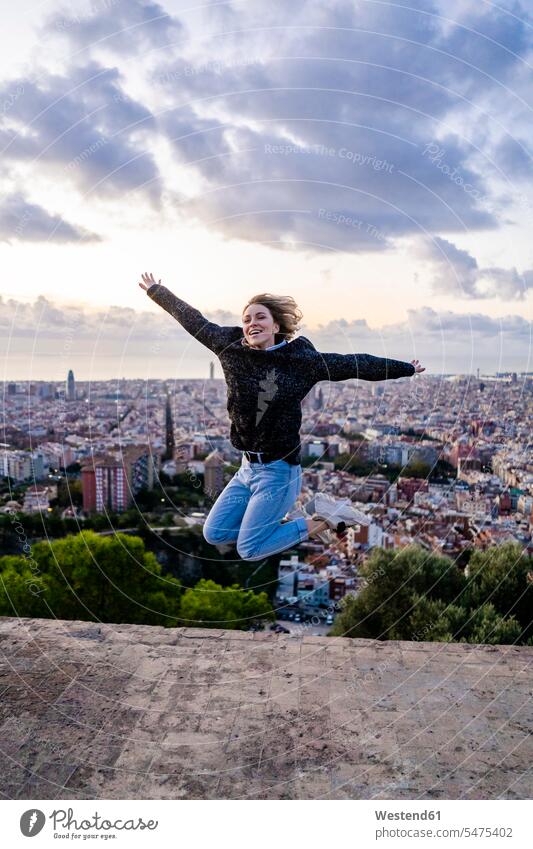 Unbeschwerte junge Frau springt bei Sonnenaufgang über die Stadt, Barcelona, Spanien Leute Menschen People Person Personen Europäisch Kaukasier kaukasisch 1 Ein