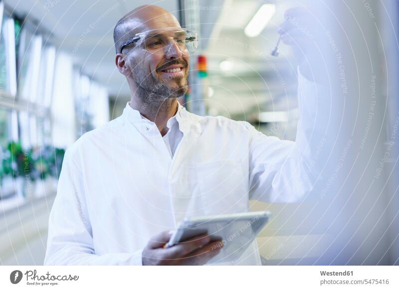 Lächelnder männlicher Wissenschaftler betrachtet Probe, während er ein digitales Tablet in der Fabrik hält Farbaufnahme Farbe Farbfoto Farbphoto Innenaufnahme