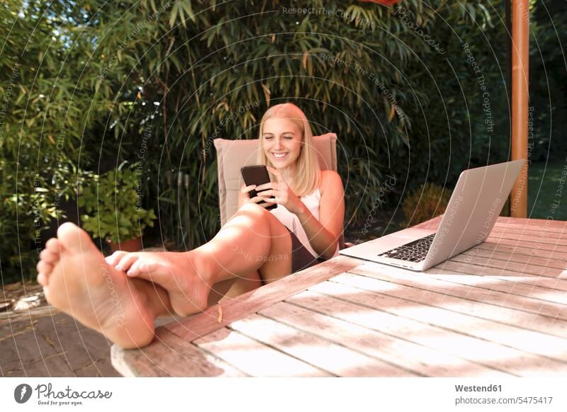 Junge Frau benutzt Smartphone im Garten sitzen sitzend sitzt lachen Gärten Gaerten iPhone Smartphones telefonieren anrufen Anruf telephonieren Freiberuflerin