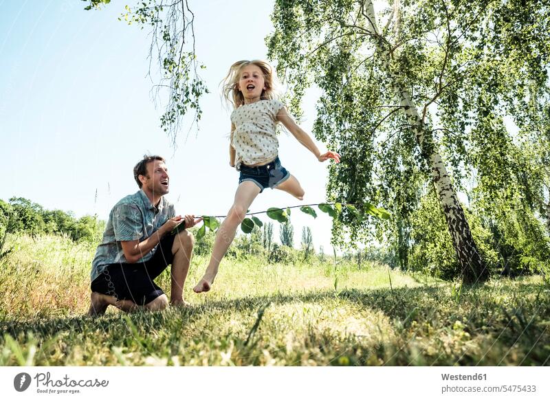 Vater mit Tochter springt über Stock in Mohnwiese Leute Menschen People Person Personen Europäisch Kaukasier kaukasisch Nordeuropäisch 2 2 Menschen 2 Personen