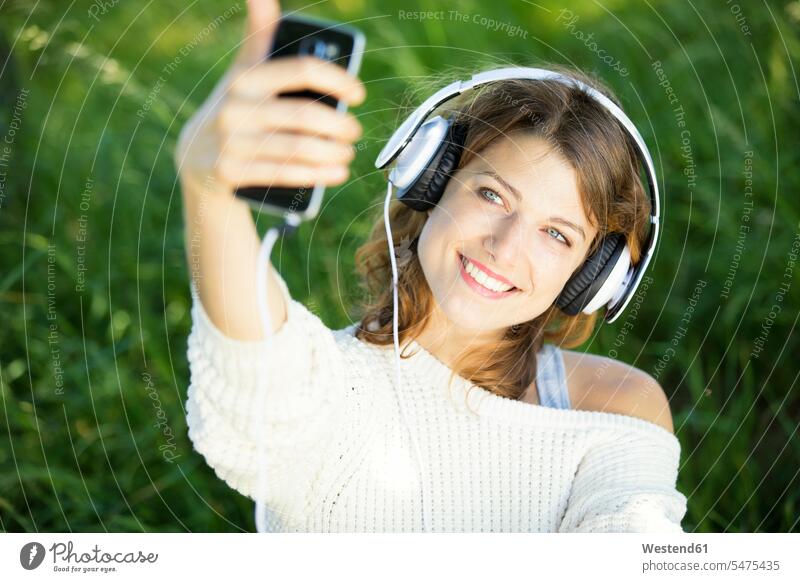 Lächelnde junge Frau mit Kopfhörern, die ein Selfie macht lächeln Kopfhoerer Musik Selfies Smartphone iPhone Smartphones fotografieren weiblich Frauen Handy