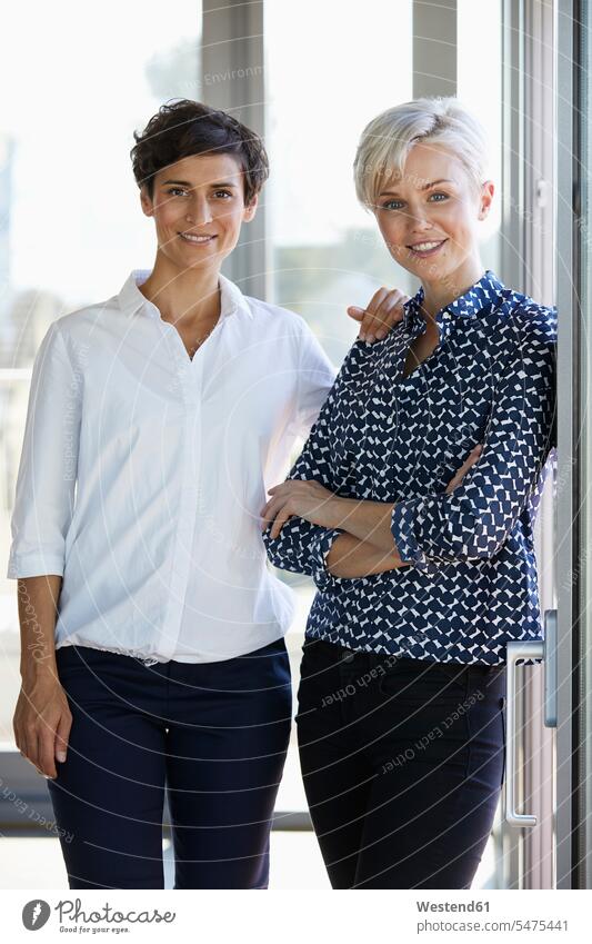 Porträt von zwei lächelnden Geschäftsfrauen am Fenster im Büro Office Büros Portrait Porträts Portraits Businesswomen Businessfrauen Businesswoman Arbeitsplatz