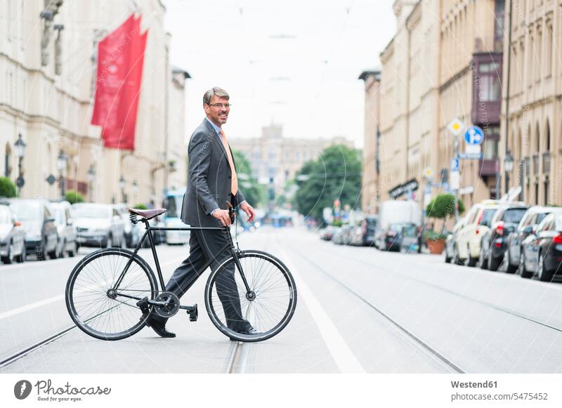 Geschäftsmann im Anzug mit Fahrrad über die Straße in der Stadt Farbaufnahme Farbe Farbfoto Farbphoto Deutschland Außenaufnahme außen draußen im Freien Tag