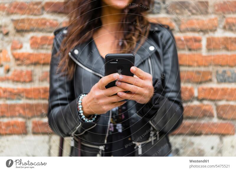 Junge Frau in schwarzer Lederjacke, mit Smartphone, Backsteinmauer im Hintergrund Backsteinwand Backsteinmauern Lederjacken iPhone Smartphones benutzen benützen