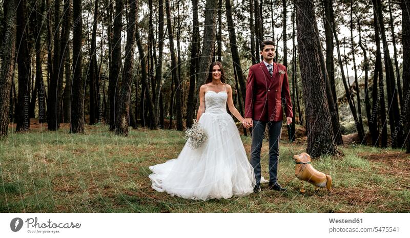Glückliche Braut und Bräutigam stehen im Wald mit lustigem Ballon in Hundeform witzig Bräute Hochzeit heiraten Heirat Hochzeiten Forst Wälder Brautpaar