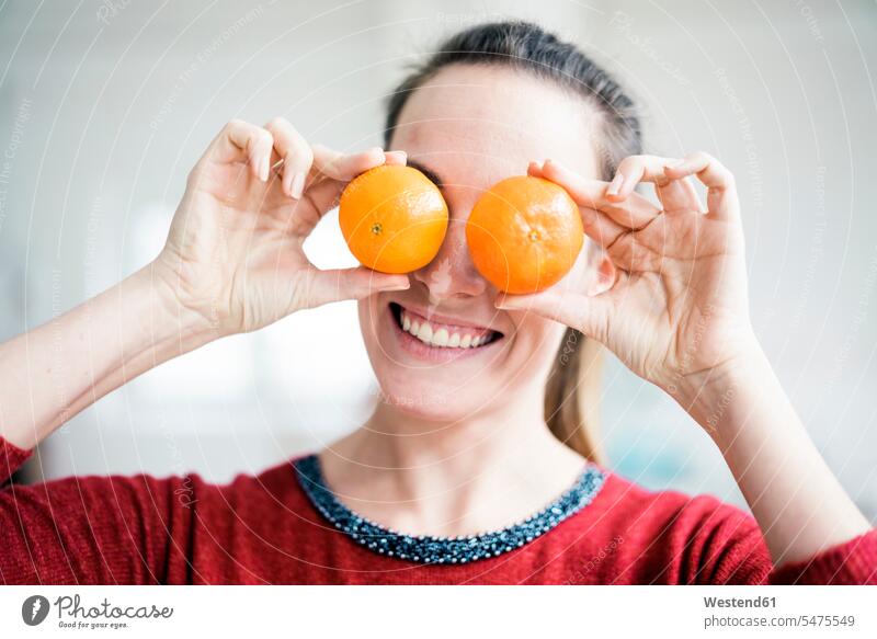 Lachende Frau, die ihre Augen mit Orangen bedeckt bedecken abdecken zudecken Citrus sinensis Apfelsinen weiblich Frauen lachen Zitrusfrucht Zitrusfruechte