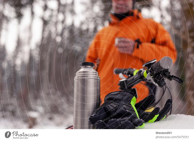 Mann, der eine Pause von einer Mountainbike-Tour im Winterwald macht und ein heißes Getränk zu sich nimmt Ausflug Ausflüge Kurzurlaub Ausfluege Mountainbiker