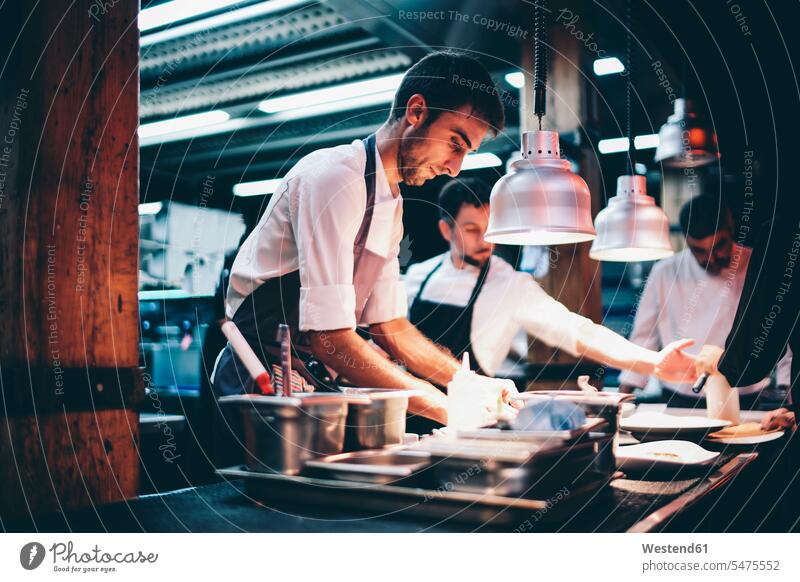 Koch, der in der Küche eines Restaurants Speisen auf einem Teller serviert Job Berufe Berufstätigkeit Beschäftigung Jobs Gastronomie Koeche Kuechenchef