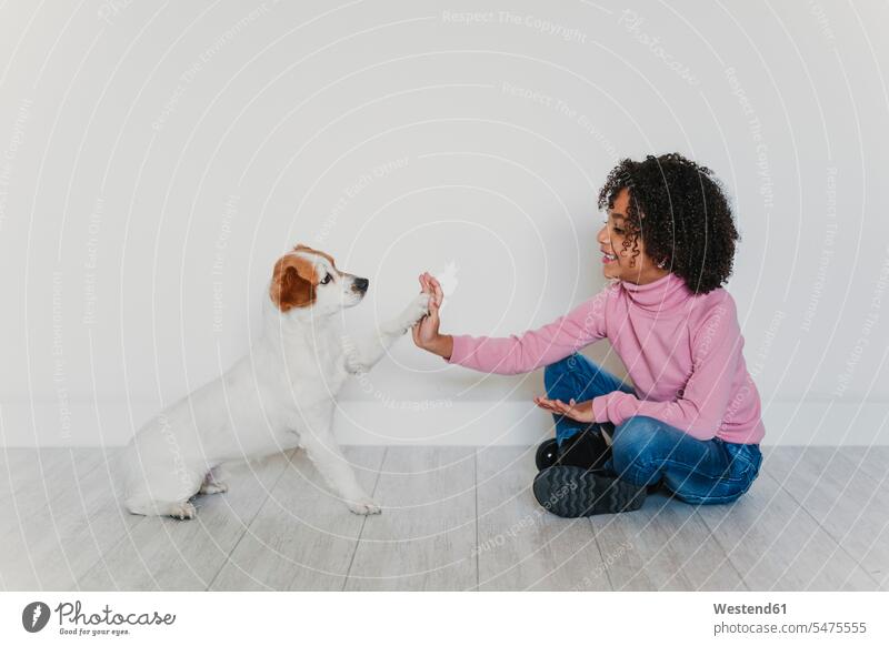 Lächelndes kleines Mädchen, das mit seinem Hund auf dem Boden sitzt und Pfötchen gibt Leute Menschen People Person Personen 1 Ein ein Mensch nur eine Person