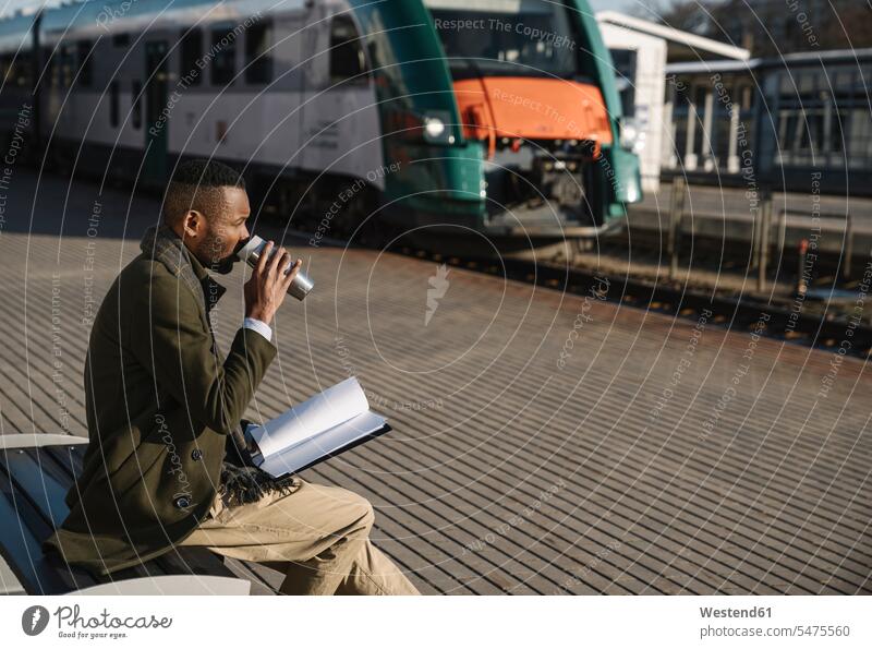 Stilvoller Geschäftsmann trinkt beim Warten auf den Zug Heißgetränk aus wiederverwendbaren Bechern Job Berufe Berufstätigkeit Beschäftigung Jobs geschäftlich