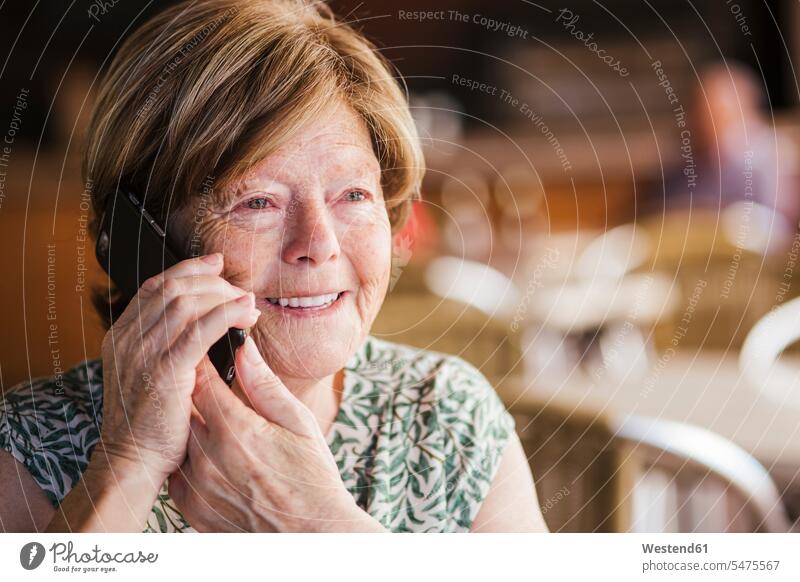 Lächelnde Frau, die im Café sitzt und mit dem Handy telefoniert Farbaufnahme Farbe Farbfoto Farbphoto Innenaufnahme Innenaufnahmen innen drinnen Handys