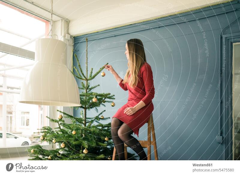 Frau sitzt auf einer Leiter in einem Loft und schmückt den Weihnachtsbaum Lofts Weihnachten Christmas X-Mas X mas Christbaum Weihnachtsbäume Weihnachtsbaeume