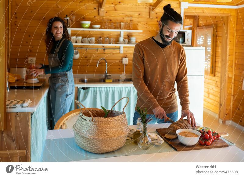 Junger Mann mit Freundin in einer Holzhütte beim Brotschneiden Touristen Schale Schalen Schälchen Schüsseln freuen geniessen Genuss Glück glücklich sein