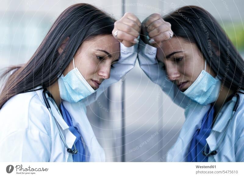 Müde Ärztin mit Gesichtsmaske an Glaswand des Krankenhauses gelehnt Farbaufnahme Farbe Farbfoto Farbphoto Außenaufnahme außen draußen im Freien Tag