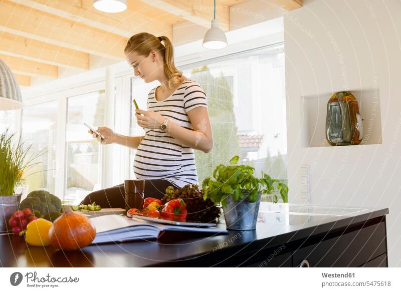 Schwangere Frau in häuslicher Küche mit Mobiltelefon Zuhause zu Hause daheim Handy Handies Handys Mobiltelefone weiblich Frauen schwanger schwangere Frau