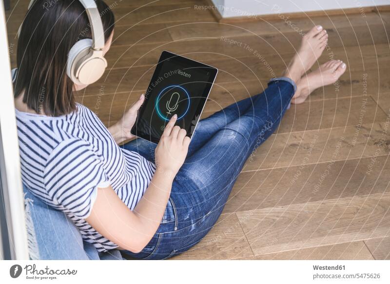 Junge Frau mit Tablet mit Smart-Home-Steuerungsfunktionen und Kopfhörer Kopfhoerer Displays hoeren sitzend sitzt daheim zu Hause entwickeln Entwicklungen Muße