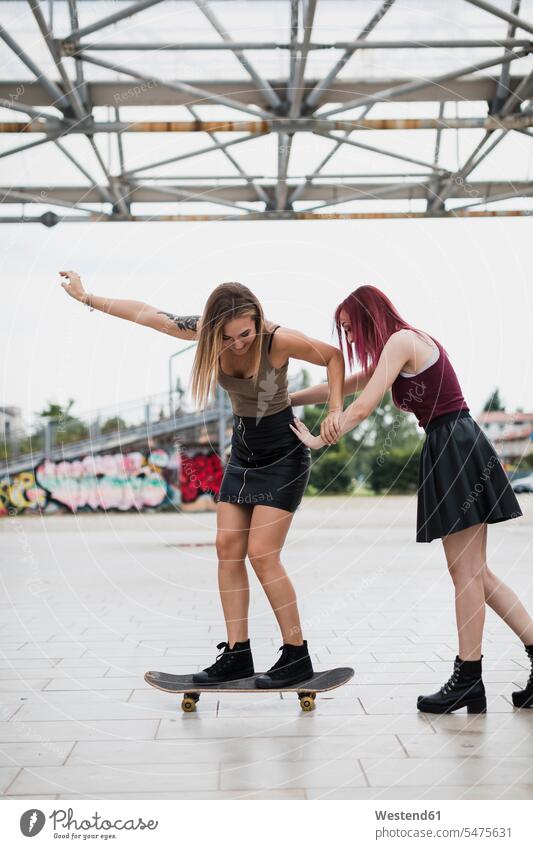 Junge Frau schiebt Freund auf Skateboard in der Stadt Freundinnen Rollbretter Skateboards schieben anschieben staedtisch städtisch weiblich Frauen Spaß Spass