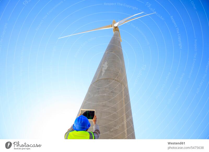Niedriger Blickwinkel eines Technikers, der mit einem Tablett einer Windkraftanlage fotografiert Windturbine Windrad Windräder fotografieren Tablet Computer