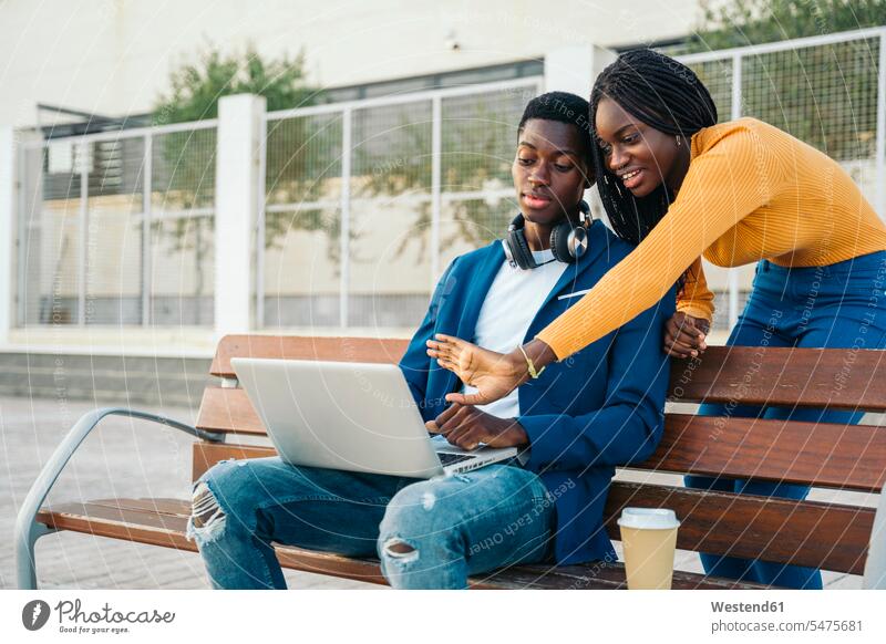 Lächelndes Teenager-Mädchen gestikuliert am Laptop, während es mit seinem Freund spricht Farbaufnahme Farbe Farbfoto Farbphoto Außenaufnahme außen draußen