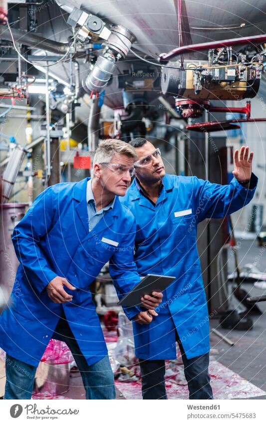 Männliche Mitarbeiter mit digitalem Tablet diskutieren bei der Prüfung von Maschinen in einer Fabrik Farbaufnahme Farbe Farbfoto Farbphoto Innenaufnahme