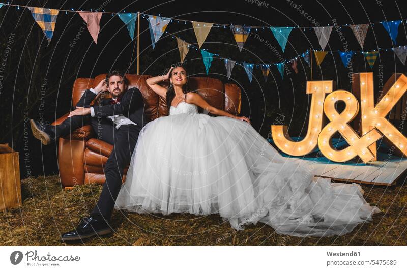 Porträt eines Hochzeitspaares, das auf einem Sofa sitzend auf einer nächtlichen Feldfeier posiert heiraten Heirat Hochzeiten Portrait Porträts Portraits sitzt