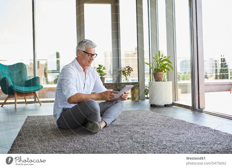Reifer Mann sitzt auf Teppich zu Hause mit Tablette Zuhause daheim Tablet Computer Tablet-PC Tablet PC iPad Tablet-Computer Männer männlich entspannt