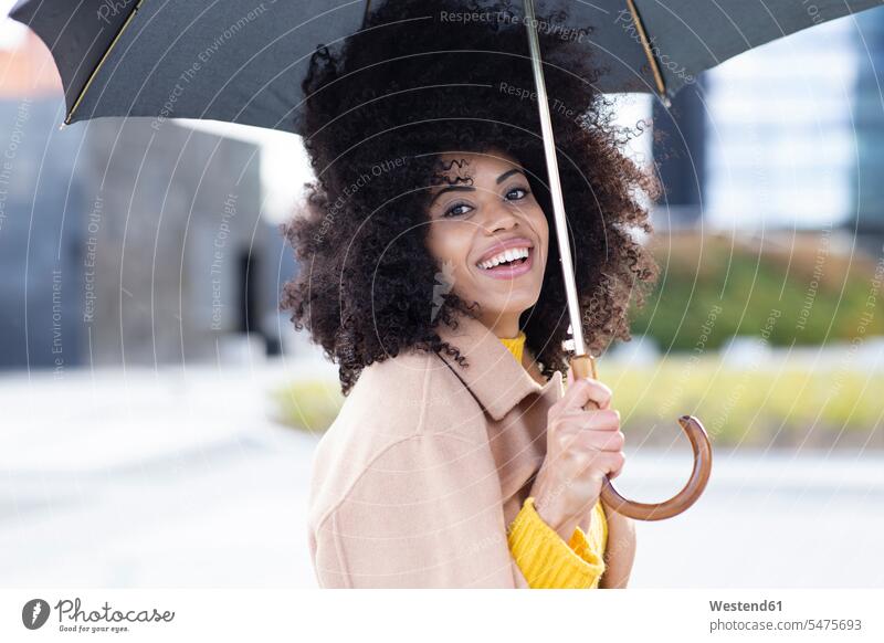 Lächelnde Frau mit Jacke, die einen Regenschirm hält, während sie im Freien steht Farbaufnahme Farbe Farbfoto Farbphoto Außenaufnahme außen draußen Tag