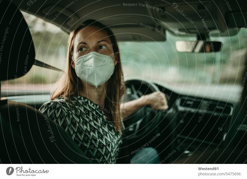 Mittlere erwachsene Frau mit Schutzmaske im Auto KFZ Verkehrsmittel Automobil Autos PKW PKWs Wagen fahrend fahrende fahrender fahrendes sitzend sitzt Muße