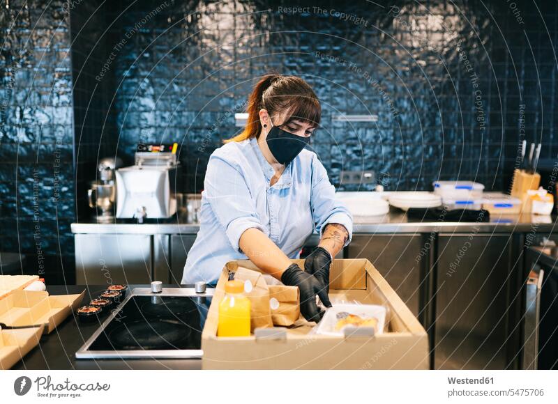 Köchin trägt Gesichtsmaske, während sie an der Restaurantküchentheke Essen in einem Pappkarton aufbewahrt Farbaufnahme Farbe Farbfoto Farbphoto Innenaufnahme