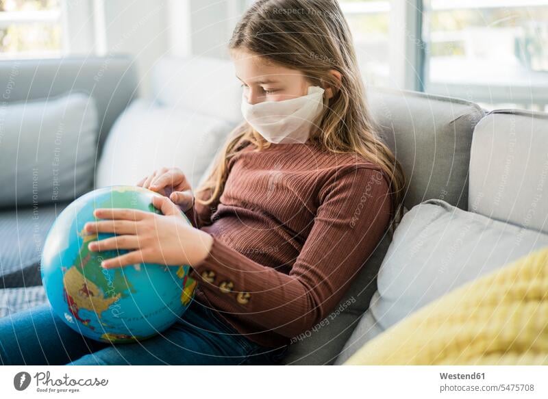 Mädchen liest den Globus, während sie zu Hause auf dem Sofa eine Gesichtsmaske trägt Farbaufnahme Farbe Farbfoto Farbphoto Innenaufnahme Innenaufnahmen innen