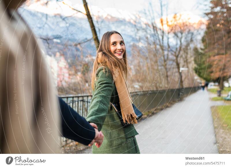 Österreich, Innsbruck, Porträt einer glücklichen jungen Frau, die im Winter Hand in Hand mit ihrem Freund spazieren geht Portrait Porträts Portraits Winterzeit