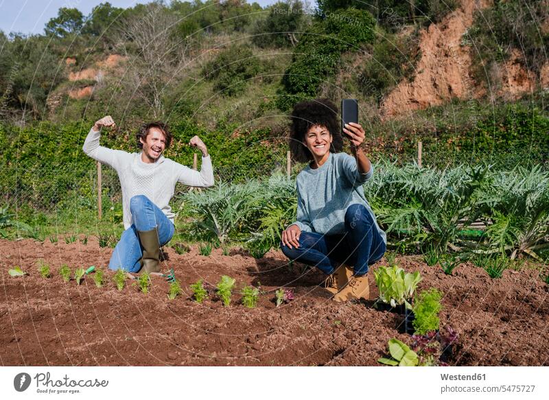 Ein Paar macht Selfies vom Pflanzen von Salatsetzlingen in einem Gemüsegarten ländlich auf dem Land auf dem Lande bio biologisch organisch