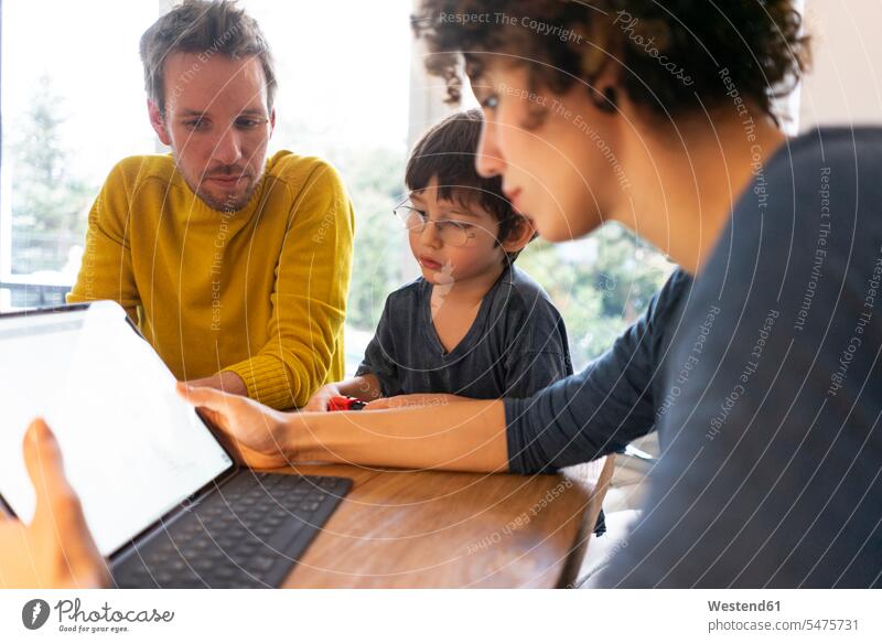 Familie sitzt am Tisch und benutzt ein digitales Tablet Gemeinsam Zusammen Miteinander Vater Papas Väter Vati Vatis Papis Mutter Mami Mutti Mütter Mama Sohn