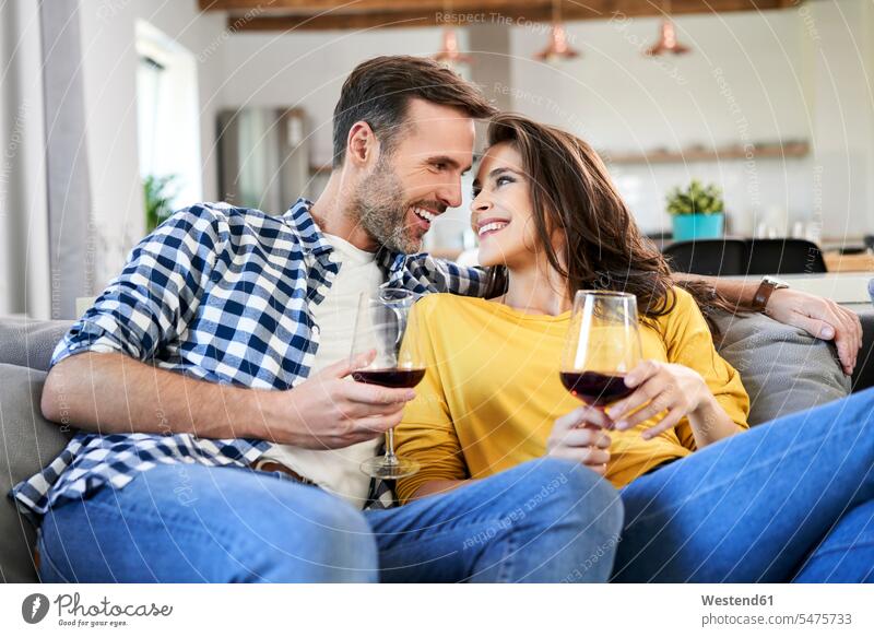 Glückliches Paar sitzt im Wohnzimmer und trinkt Rotwein Sofa Couches Liege Sofas sitzen sitzend trinken Wohnraum Wohnung Wohnen Wohnräume Wohnungen Pärchen