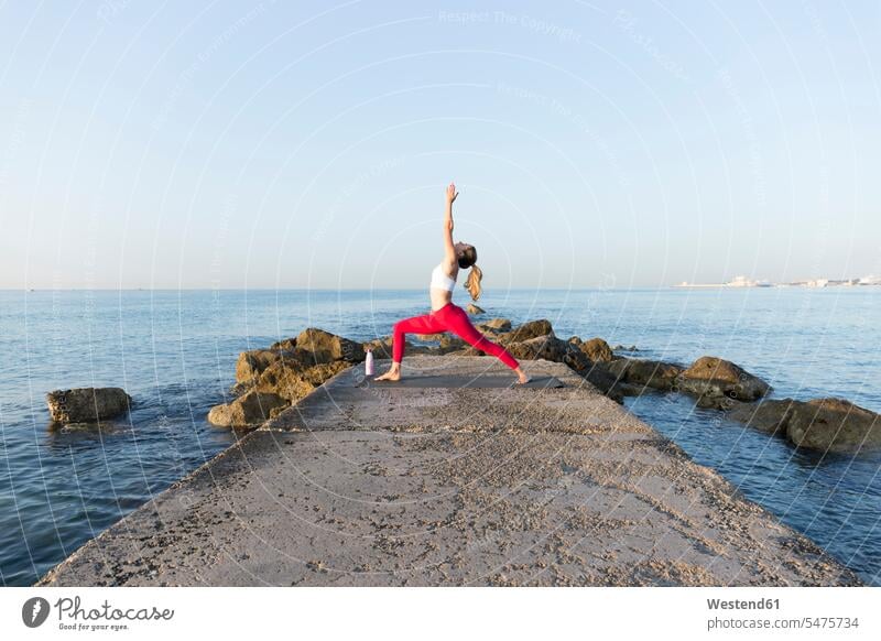 Junge Frau übt Yoga am Strand, tun Krieger Pose ausüben trainieren Übung früh Frühe Morgen anpassungsfähig Anpassungsfähigkeit flexibel kräftig stark Stärke