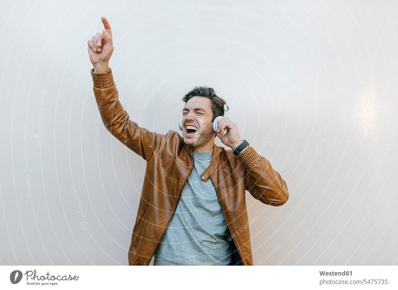 Sorgloser Mann, der mit Kopfhörern vor einer Wand Musik hört Kopfhoerer entspannen relaxen hoeren begeistert Enthusiasmus enthusiastisch Überschwang