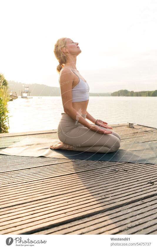 Junge Frau, die auf einem Steg an einem See Yoga praktiziert Handtuecher Handtücher entspannen relaxen ausüben trainieren Übung früh Frühe Morgen sommerlich