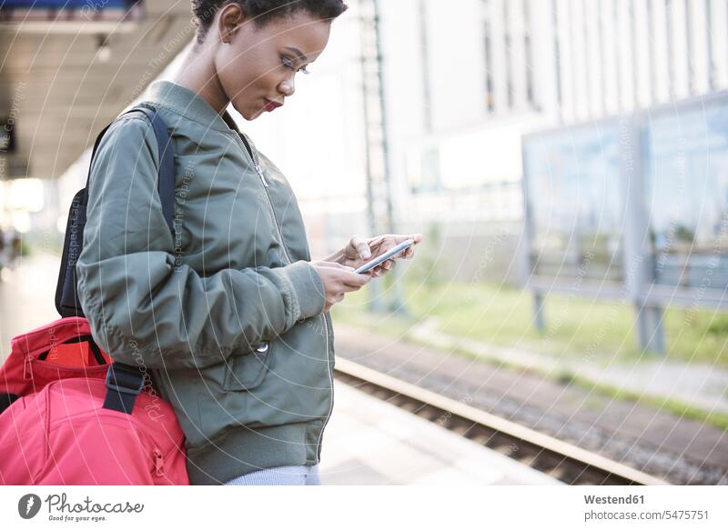 Junge Frau steht auf Bahnsteig und schaut auf Handy ansehen Smartphone iPhone Smartphones stehen stehend weiblich Frauen Zugbahnsteig Zugbahnsteige Bahnsteige
