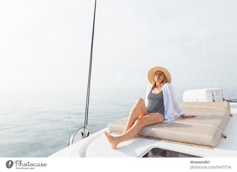 Reife Frau entspannt sich auf einem Katamaran und nimmt ein Sonnenbad sitzen sitzend sitzt reife Frau reife Frauen Schiffsdeck Decks Schiffsdecks sonnenbaden